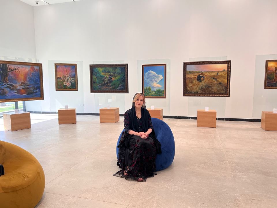 Artist Hawar Mazhar seated in the gallery among her original oil paintings